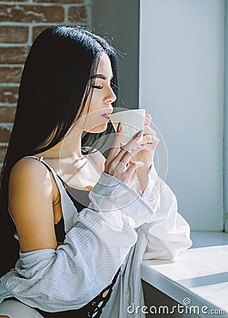 Drink well feel well. Pretty woman drinking healthy morning drink at window. Adorable girl holding cup with tasty coffee Stock Photo