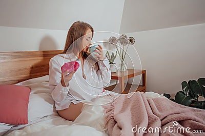 Drinking coffee and eating doughnut for breakfast in bed Stock Photo
