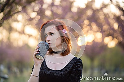 Drinking coffee from paper mug cup - Happy young travel dancer woman enjoying free time in a sakura cherry blossom park Stock Photo