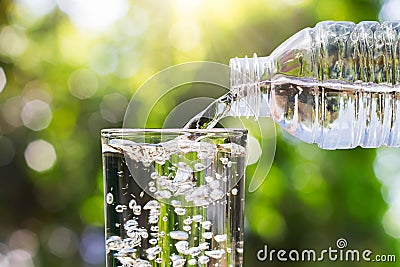 Drinking water pouring from bottle into glass on blurred fresh green nature bokeh background Stock Photo