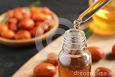 Dripping jojoba oil from pipette into bottle on blurred background Stock Photo