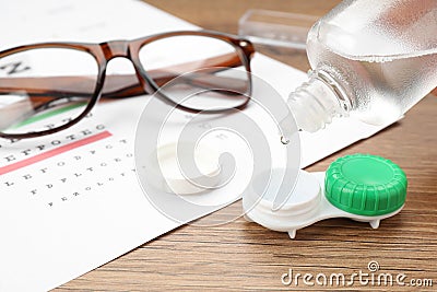 Dripping solution into case with contact lenses on wooden table, closeup Stock Photo