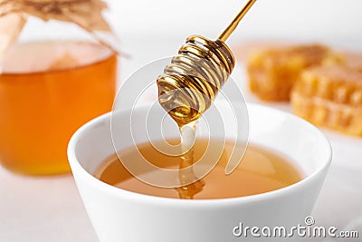 Dripping tasty honey from dipper into bowl on table, closeup Stock Photo