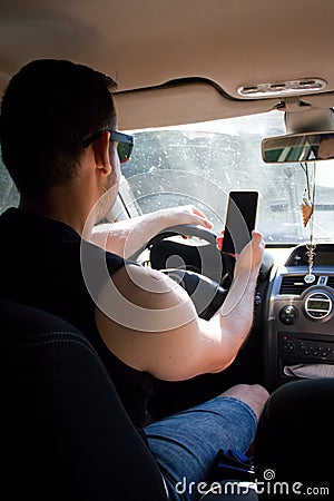 The man drives a car and uses a mobile phone at the same time. Stock Photo