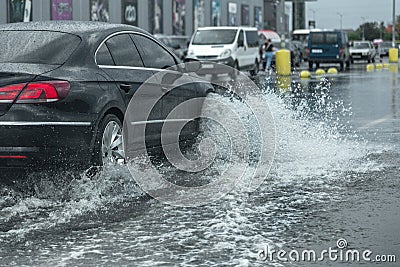 Driving car on flooded road during flood caused by torrential rains. Cars float on water, flooding streets. Splash on the car. Editorial Stock Photo