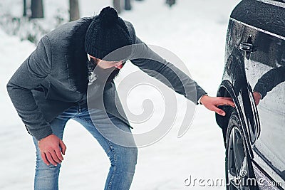 Driving a car in winter. Man checks wheels on a snowy road before driving Stock Photo