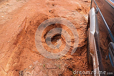 Driving 4wd vehicle on red dusty country road with big holes, detail on tire going over rough pothole terrain. Roads are in bad Stock Photo