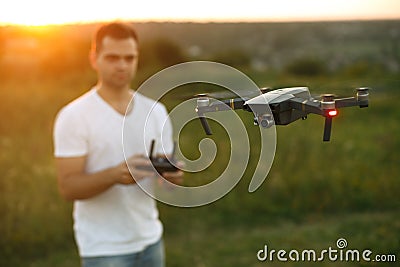 Drone hovers in front of man with remote controller in his hands. Quadcopter flies near pilot. Guy taking aerial photos Stock Photo