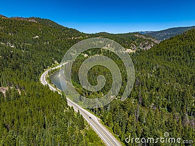 Drone view of Crowsnest Highway by river passing through rocks, dense forests and mountains, Canada. Stock Photo