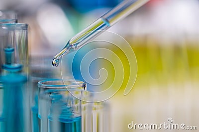 Drop of blue liquid from droper droping to test tube in laboratory with bright color blur background Stock Photo