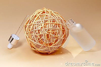 Dropper bottle made of white frosted glass and pipette leaned on the wicker rattan ball Stock Photo