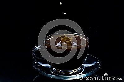 Drops of milk fall into a glass cup with black coffee, black background Stock Photo