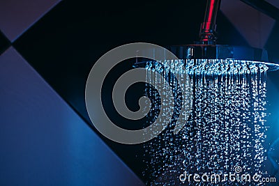 Drops of water fall from a watering can in the shower in blue light. Water drops close-up. Flow of water. Stock Photo