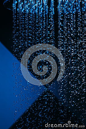 Drops of water fall from a watering can in the shower in blue light. Water drops close-up. Flow of water. Stock Photo