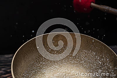 Drops of water fly into the air from hitting a Tibetan & x28;singing& x29; bowl. Cold boil. Tibetan bowl on a black Stock Photo