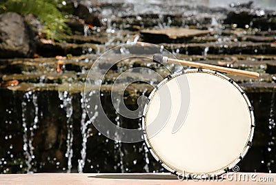 Drum with mallet near waterfall outdoors on sunny day, space for text. Percussion musical instrument Stock Photo