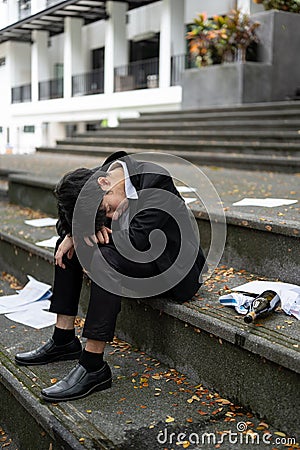 A drunk, hopeless Asian businessman sits on the stairs in front of the building after getting fired Stock Photo