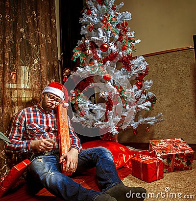 Drunk nerd in santa hat lying under the Christma tree with a lot Stock Photo
