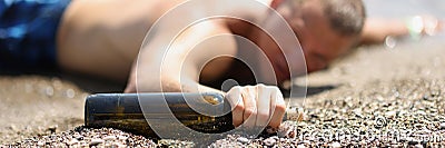 Drunk young man lying on seashore with bottle of wine in his hands closeup Stock Photo