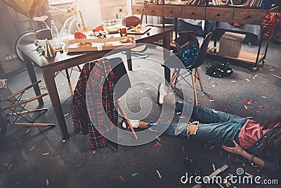 Drunk young woman lying on floor in messy room after party Stock Photo