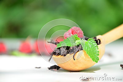 dry black tea in a wooden spoon on a white plate with raspberries and mint. healthy healing berry tea Stock Photo