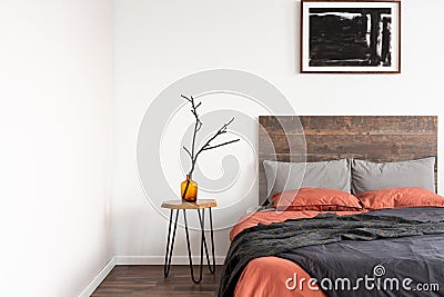 Dry branch in glass vase on wooden nightstand table nest to king size bed with orange and grey bedding Stock Photo