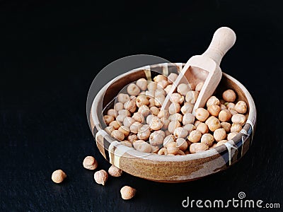 Dry chickpea beans in bowl with wooden scoop over black background Stock Photo