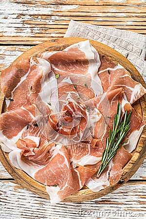 Dry cured parma ham or Prosciutto crudo on a wooden board with rosemary. White wooden background. Top View Stock Photo