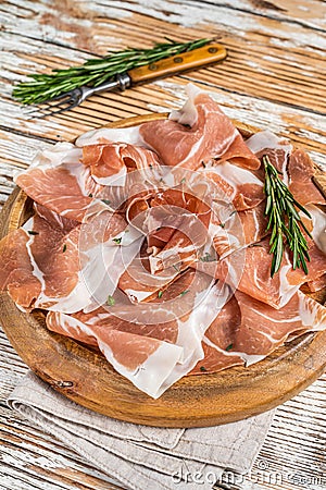Dry cured parma ham or Prosciutto crudo on a wooden board with rosemary. White wooden background. Top View Stock Photo