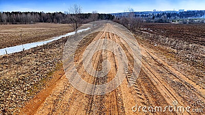 A dry dirt clay rural road in a field, stretching to the horizon in early spring. Rustic landscape Stock Photo