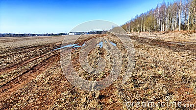 A dry dirt clay rural road in a field, stretching to the horizon in early spring. Rustic landscape Stock Photo
