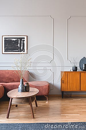 Dry flowers in stylish dark vase on wooden coffee table in front of ginger colored corner sofa Stock Photo