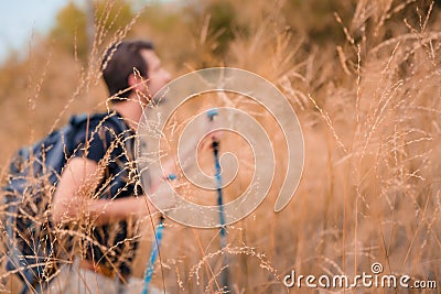 Dry grass flowers with blurred background of caucasian man hiker having fun walking up mountain on trail with dry grass field in Stock Photo