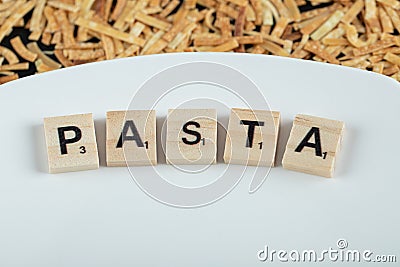 Dry pasta scattered around white plate with wooden letters Editorial Stock Photo