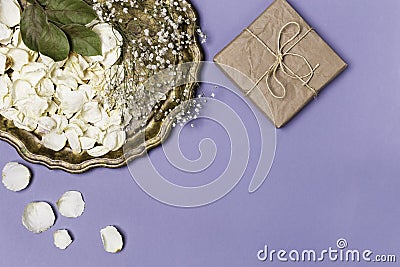 Dry petals of white roses and gypsophila on a beautiful antique tray, a gift wrapped in craft paper on a blue background. Place Stock Photo