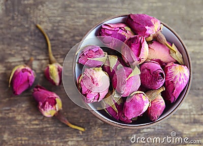 Dry rose buds flowers in a bowl on old wooden table.Healthy herbal drinks concept.Asian ingredient for aromatherapy tea. Stock Photo