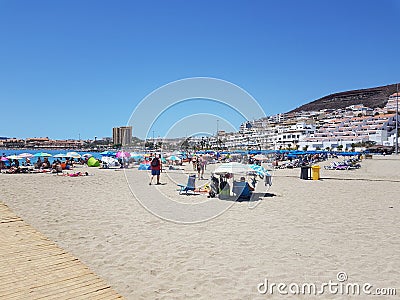 Dry sandy beach view of holiday makers sun bathing and sitting in shade under parasols Editorial Stock Photo