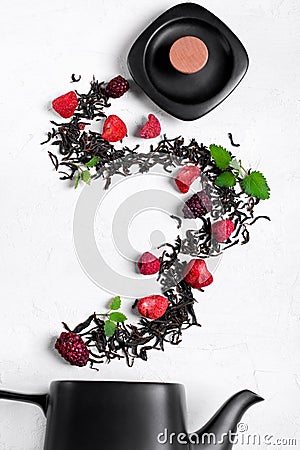 Dry tea leaves, freeze dried strawberry, raspberry and blackberry and mint flying into the black teapot Stock Photo