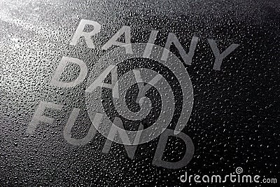 The dry words rainy day fund covered from water drops on black surface, unusual implementation concept Stock Photo