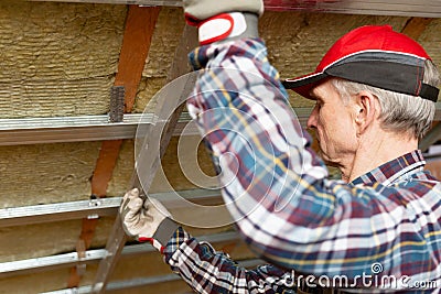 Drywall plaster wall metal fixation. Man holding metal ruler against metal frame on unfinished attic ceiling Stock Photo