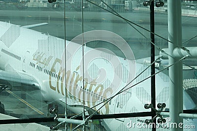 Emirates Airlines jetliner parked on apron viewed from waiting lounge of departure gate inside the terminal at Dubai International Editorial Stock Photo