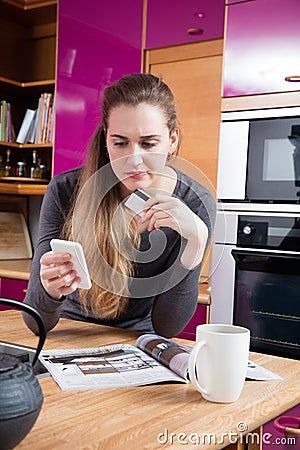 Dubious beautiful young woman shopping online from her home kitchen Stock Photo