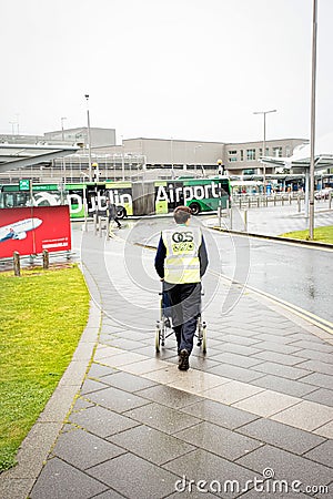 Dublin airport member staff pushing wheelchair for disabled passenger to Terminal building on summer rainy day, Dublin Airport, 14 Editorial Stock Photo