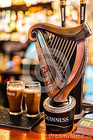 Selective focus on Guinness tap with blurred pints of foamy beer Editorial Stock Photo