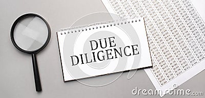 due diligence sign in white paper notepad and magnifying glass on the grey background Stock Photo