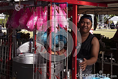 Dumaguete, Philippines - 27 July 2018: Pink cotton candy seller on market stand. Smiling Philippine man selling sweets Editorial Stock Photo