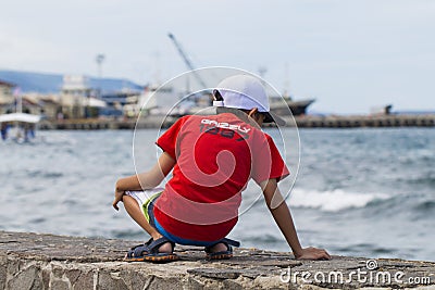 Dumaguete, Philippines - 13 May 2017: a boy in red t-shirt looks at the sea and port. Sea travel. Editorial Stock Photo