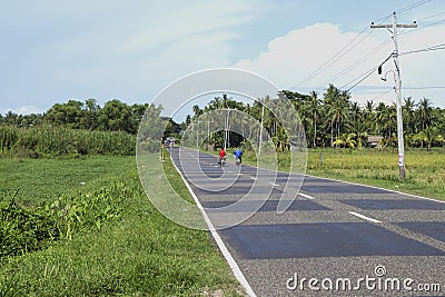 Dumaguete, Philippines - 1 Nov 2017: two bikers on empty road in rice fields. Tropical landscape. Editorial Stock Photo