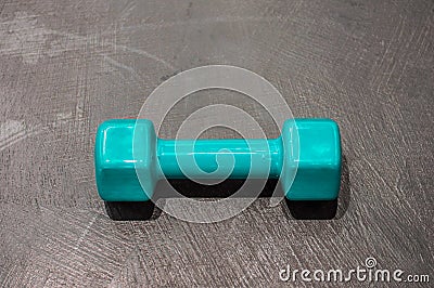 Dumbbell in a silicone shell of turquoise color on the gray floor Stock Photo