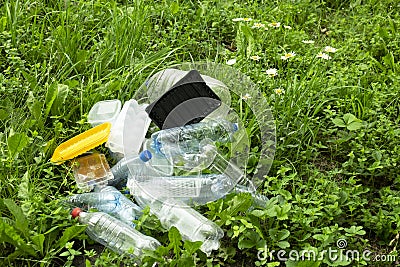 Dump of plastic garbage in the forest or in the meadow near the chamomile flowers. Plastic bottles, food containers Stock Photo